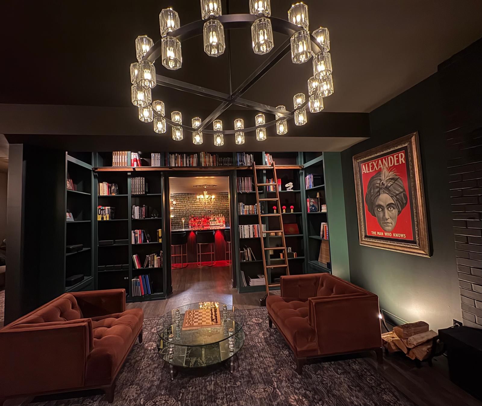 A green-shelved library with a rolling ladder and velvet armchairs