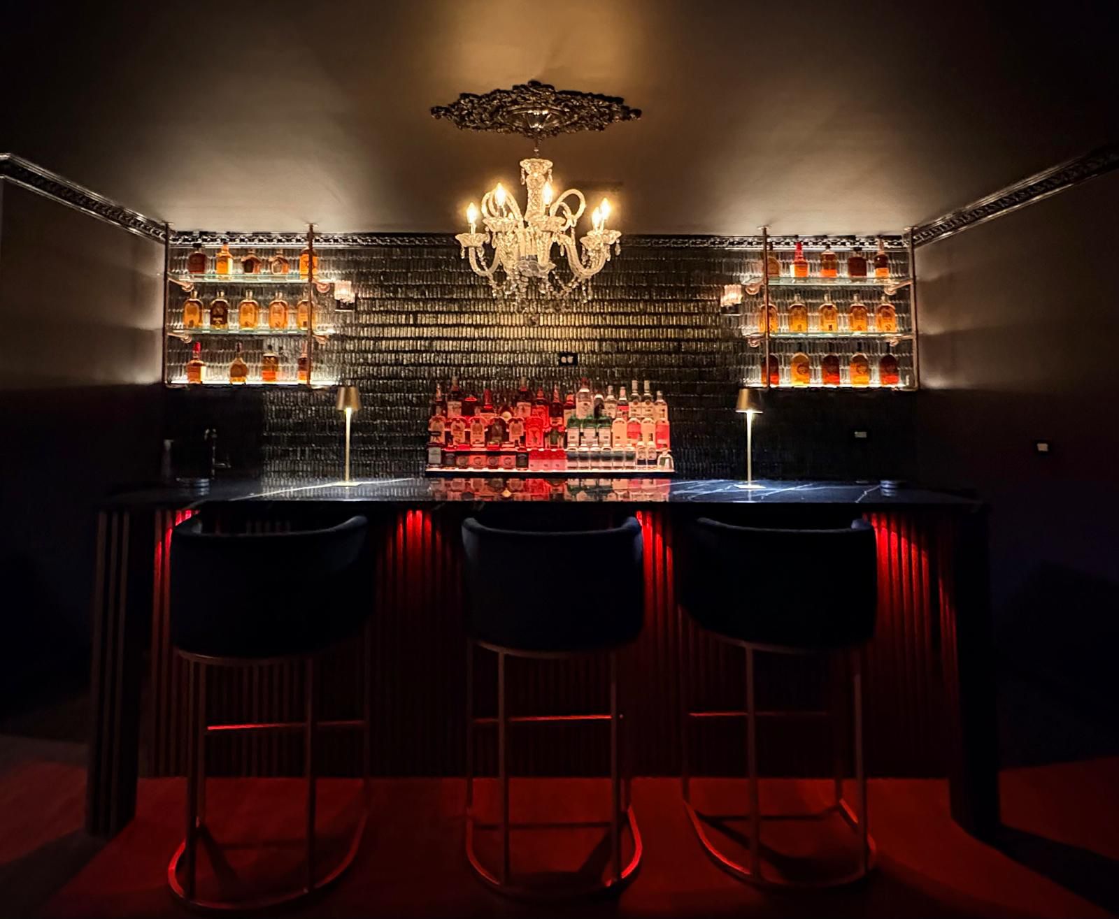 The Mansion bar, lit low with red under-counter light and a crystal chandelier